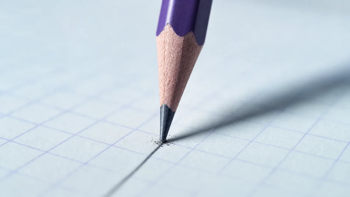 Macro photograph of a sharpened pencil tip mid-stroke on pale-blue graph paper