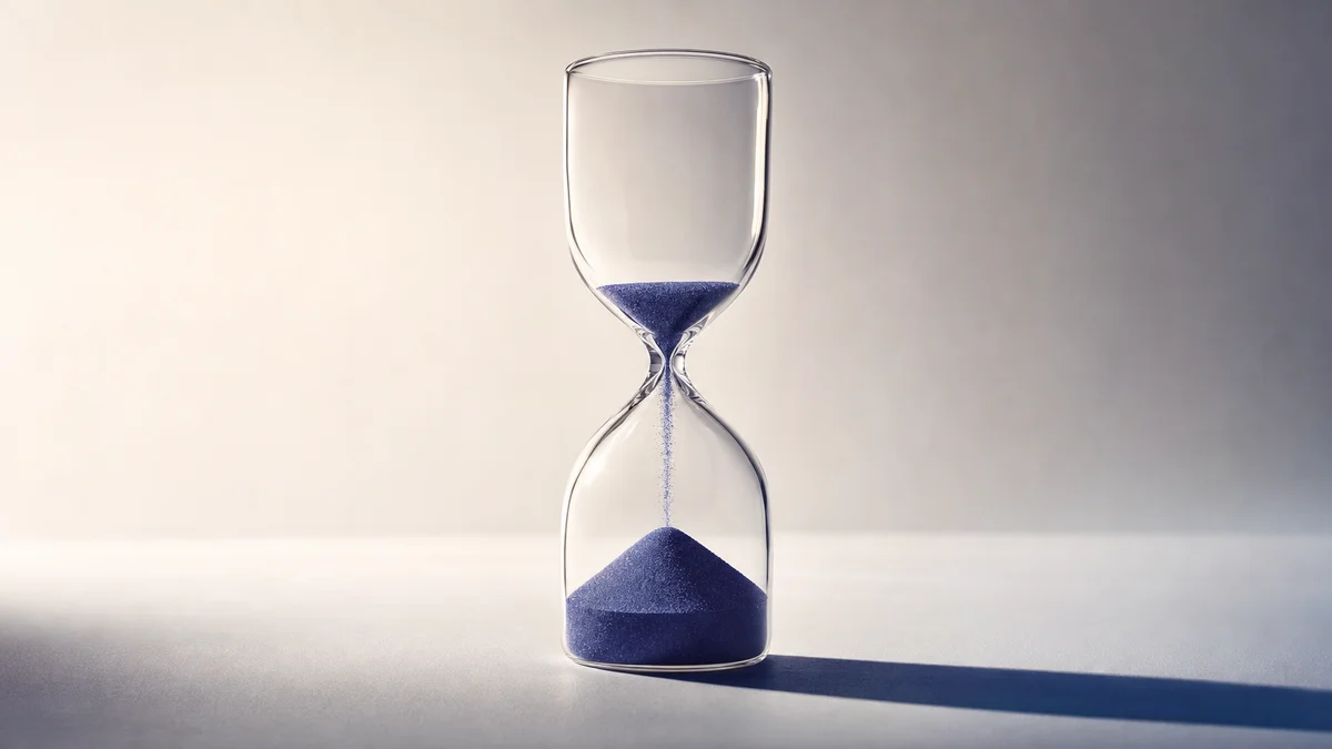 A glass hourglass with sand falling, isolated on a pale background with a single side light